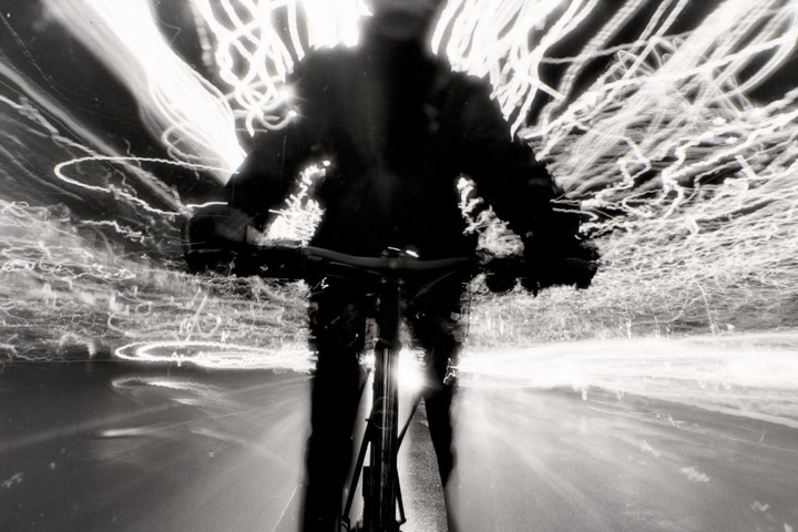 A person rides a bicycle at night, creating light trails from movement.