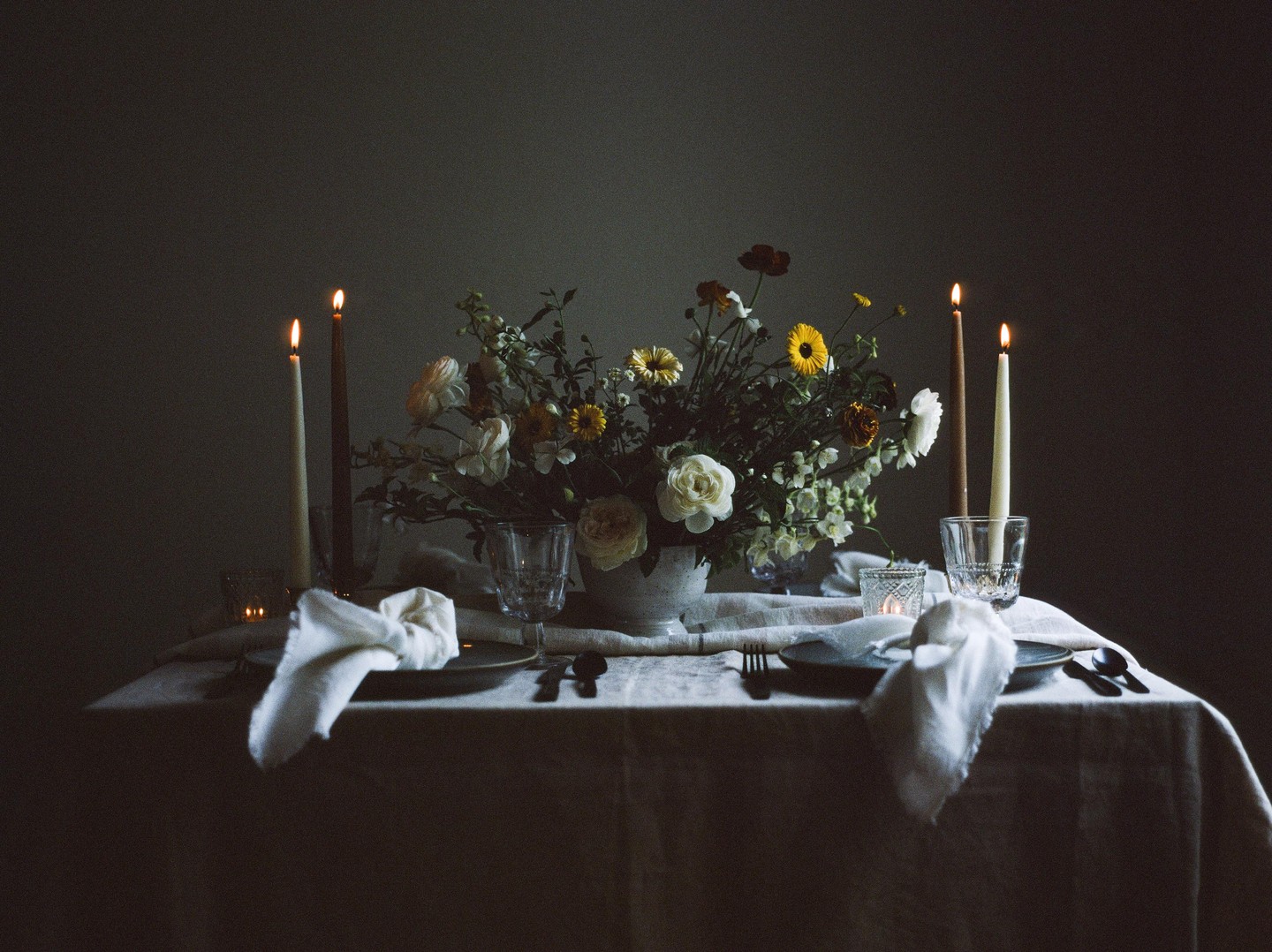 A table is set with a floral centerpiece, candles, and place settings.