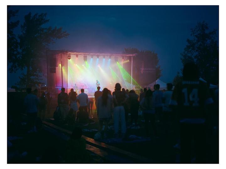 A crowd of people watches a band perform on an outdoor stage at night.