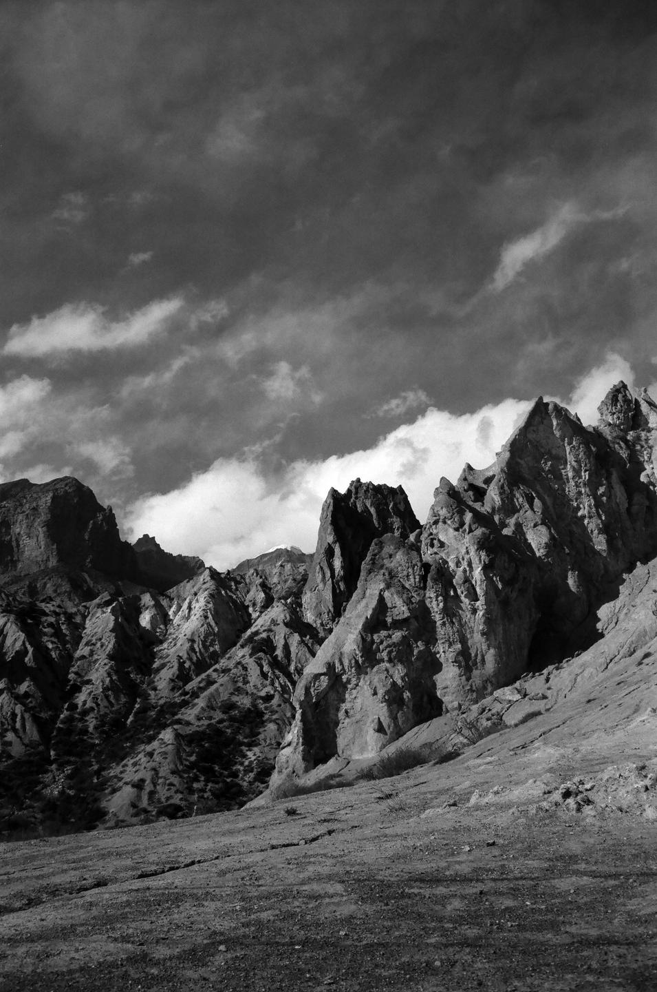 A dramatic black and white landscape shows rugged mountains under a cloudy sky.