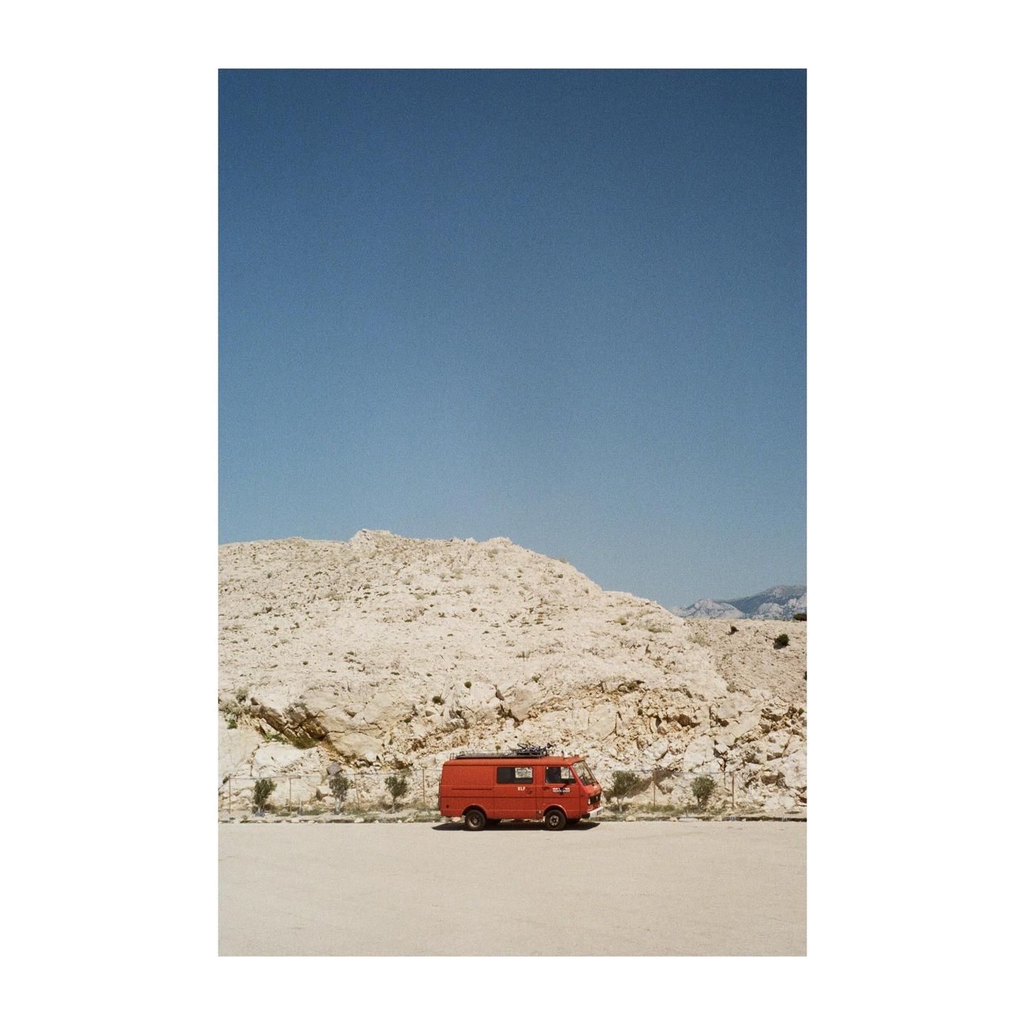 A red van is parked in front of a rocky hill under a clear blue sky.