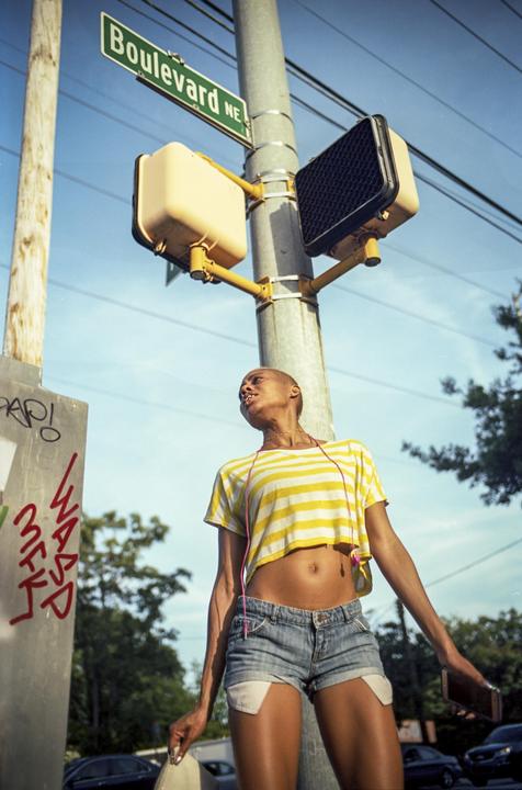 A woman wearing a striped crop top and denim shorts stands under a street sign that reads "Boulevard NE."