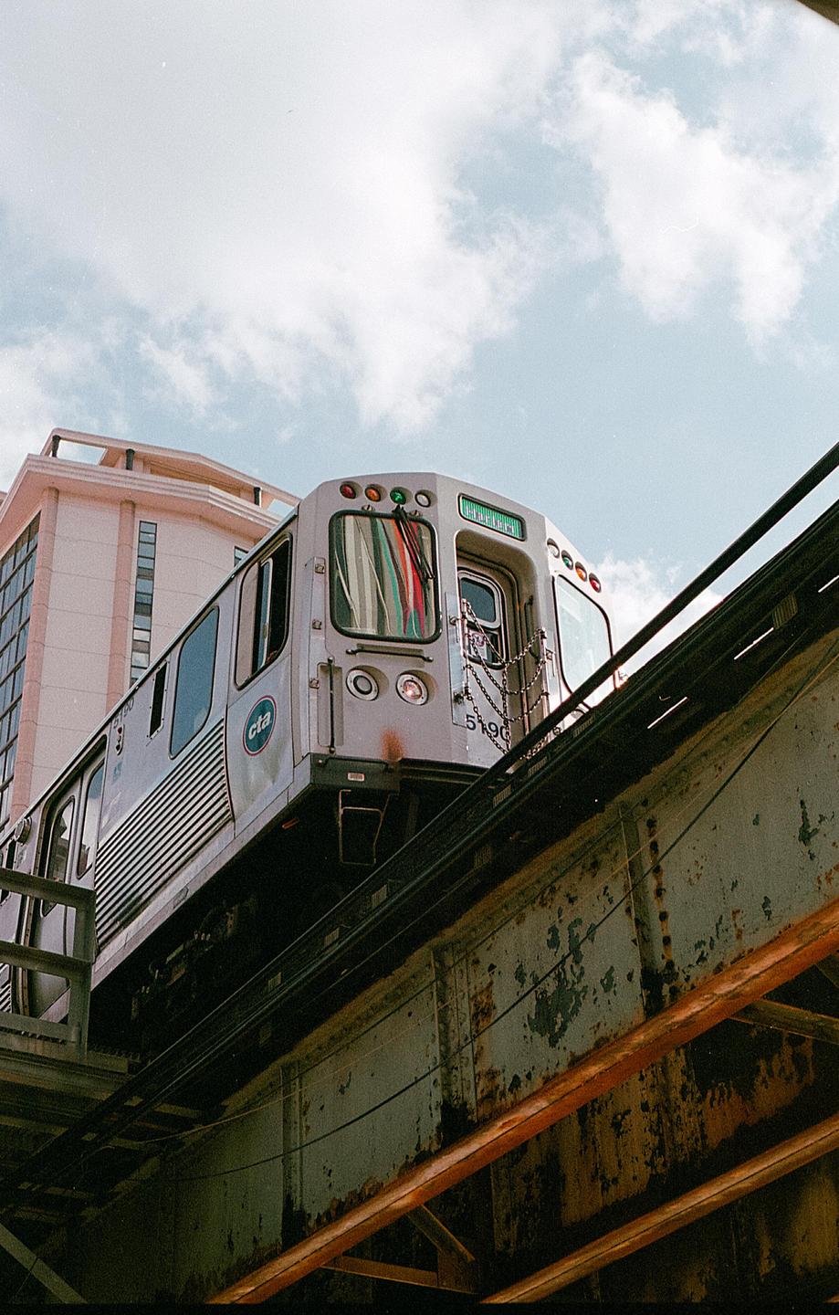 A train is visible on an elevated track with a building and cloudy sky in the background.