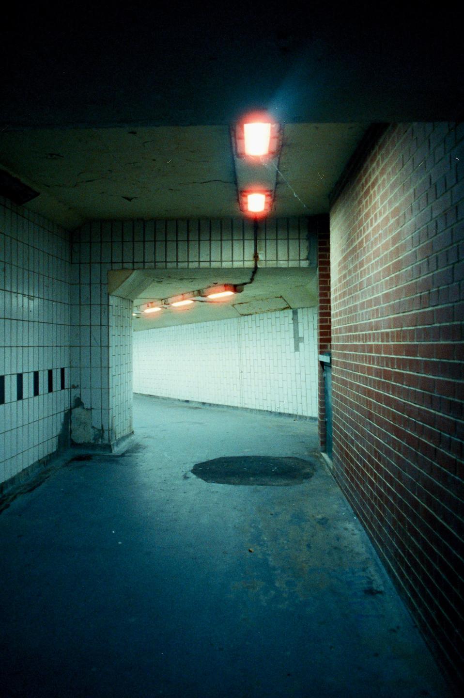 A dark, empty underpass with red lights on the ceiling and a puddle on the ground is visible.