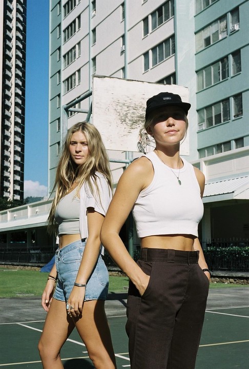 Two women stand on a basketball court in front of tall buildings.