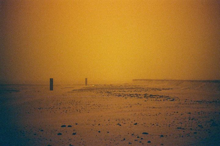 Two dark rectangular posts stand in a vast, hazy, orange-toned landscape with a distant horizon.
