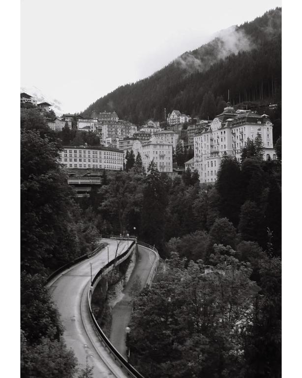 A winding road leads through a valley with buildings nestled into a forested mountain.