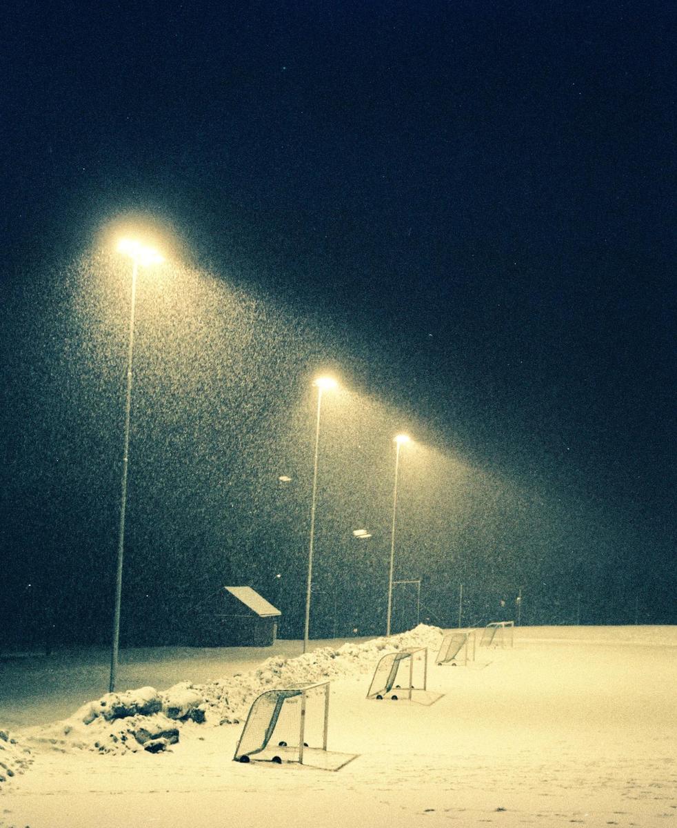 A snow-covered sports field with several small goals is illuminated by bright streetlights at night.