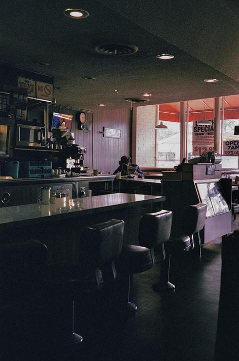 A person sits at a diner counter reading a newspaper.