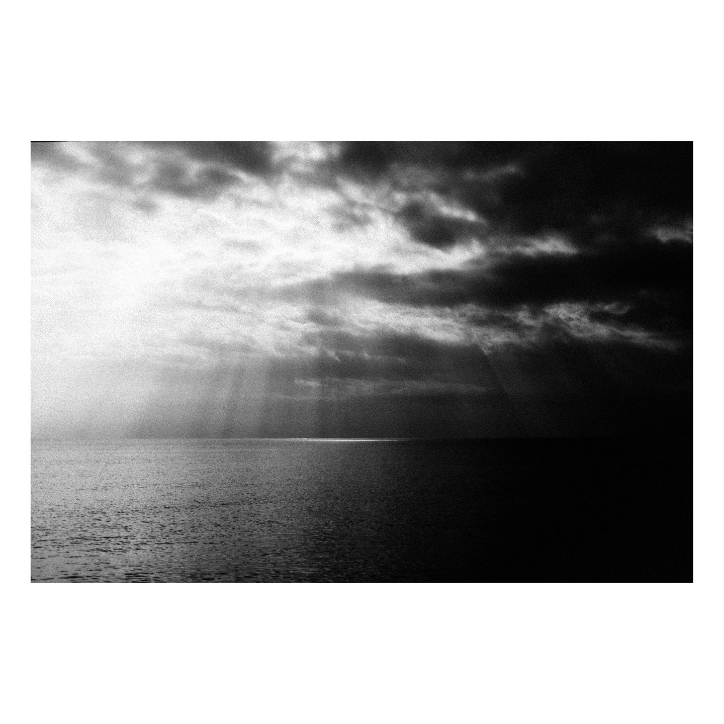 Sunlight breaks through dark clouds and illuminates a line on the ocean surface.