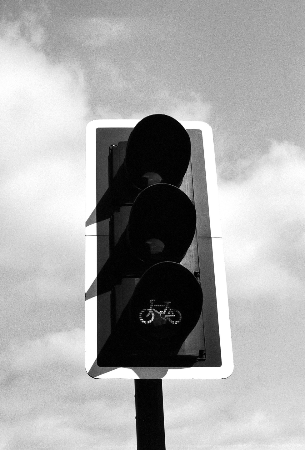 A black and white photograph shows a traffic light for bicycles against a cloudy sky.