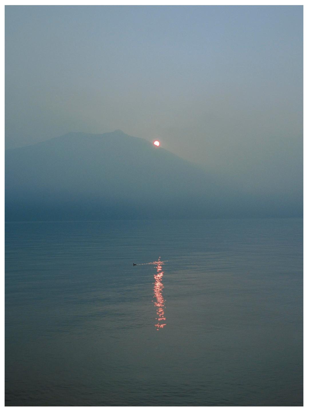 A hazy sunset over a lake with a mountain in the background and a small boat in the foreground.