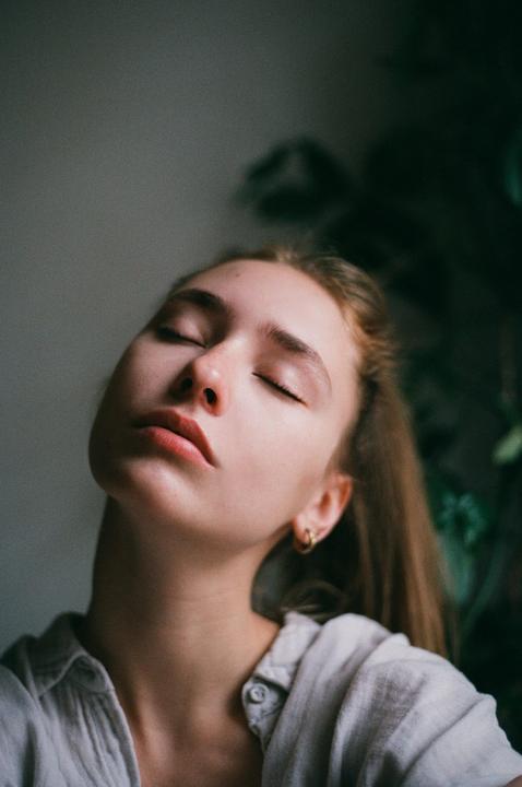 A woman with closed eyes and her head tilted back is illuminated by soft light.