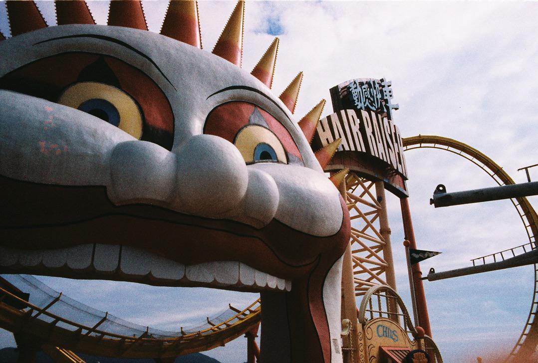 A large, colorful cartoon face with big eyes and a wide mouth is visible next to a roller coaster track and a sign that reads "HAIR RAISER."