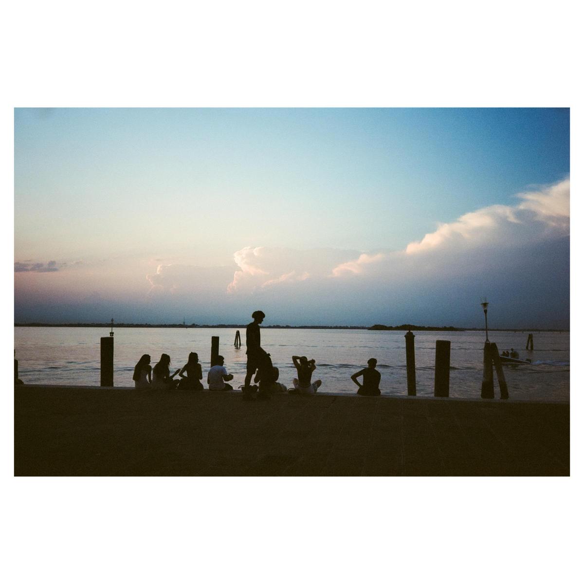 A group of people are silhouetted against the water and sky at dusk.