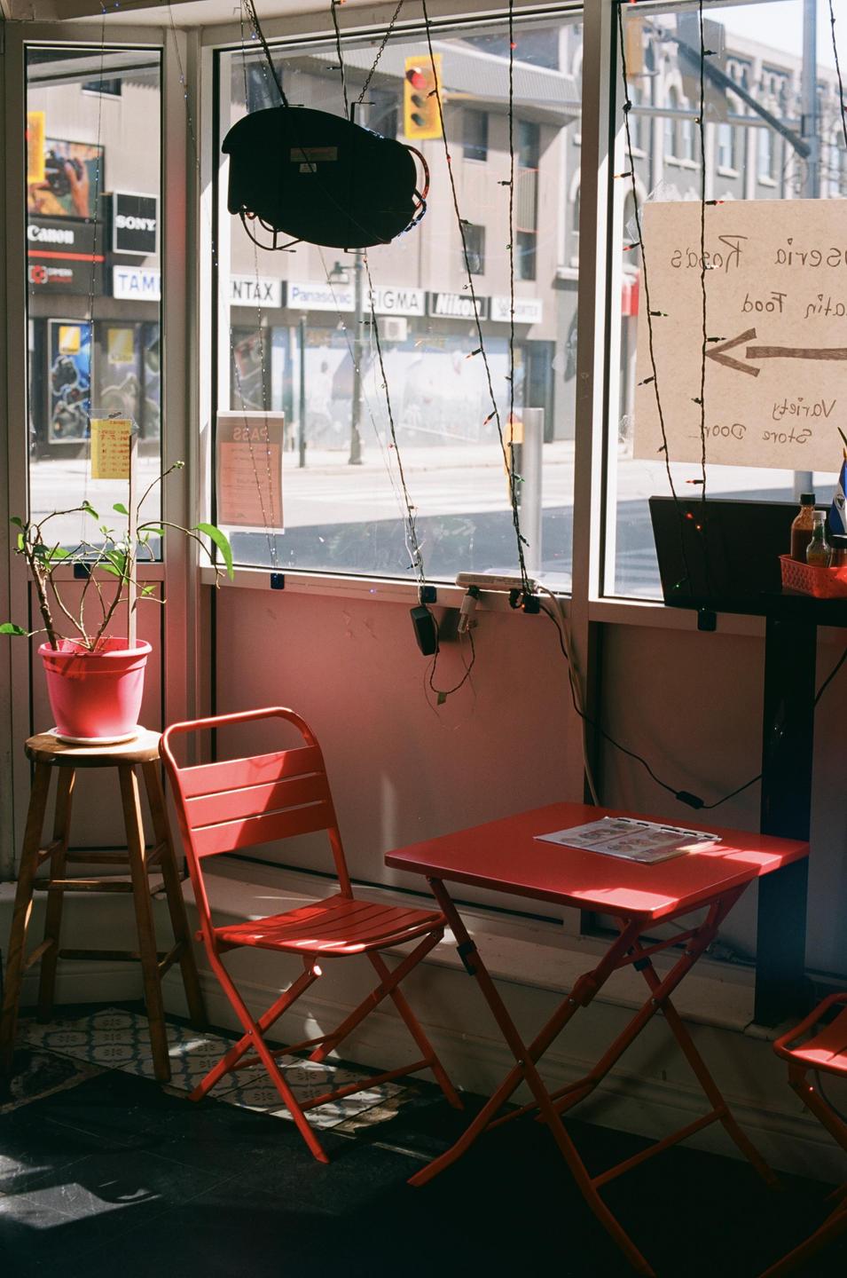 A red table and chair sit by a window looking out onto a street with buildings and a traffic light.