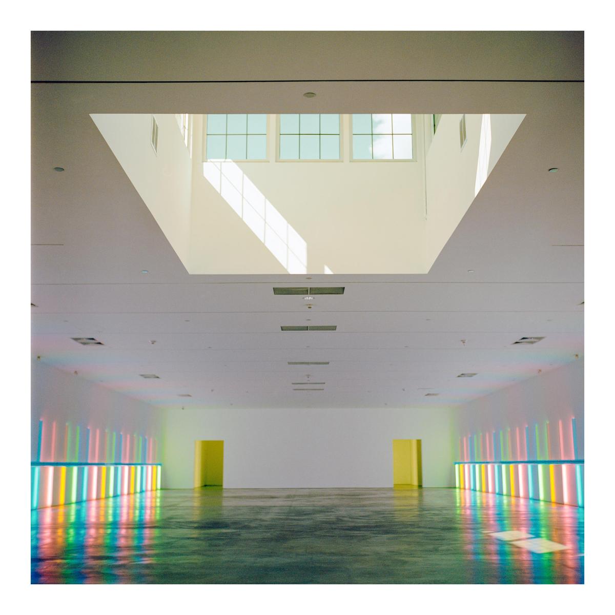 A large, empty room with a skylight and colorful neon lights reflecting on the floor is visible.