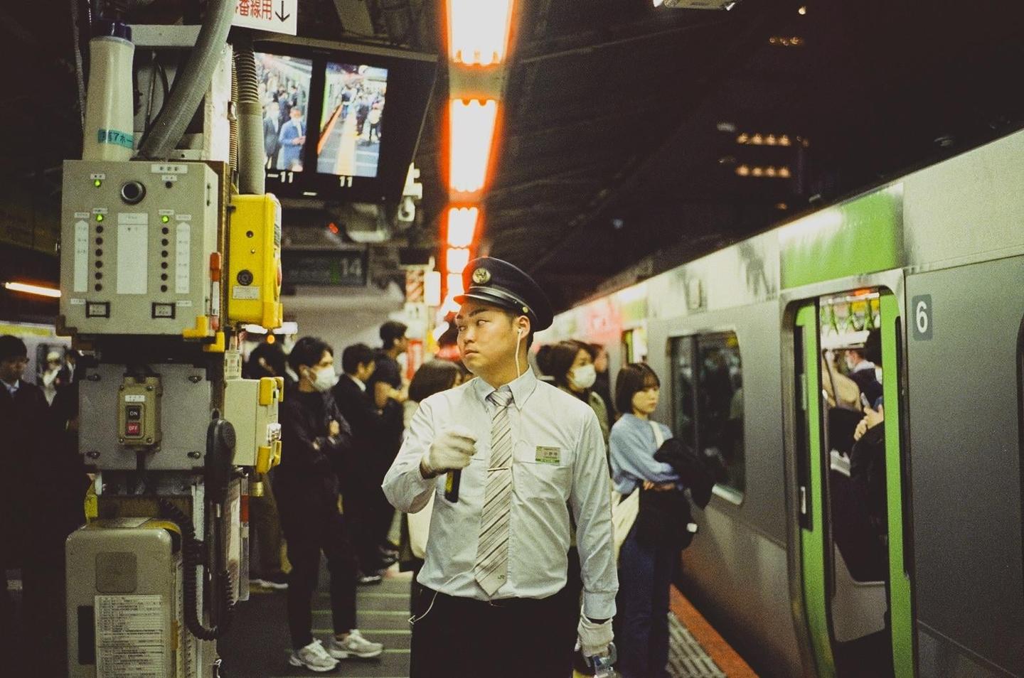 A man in a uniform stands on a subway platform next to a train with its doors open.