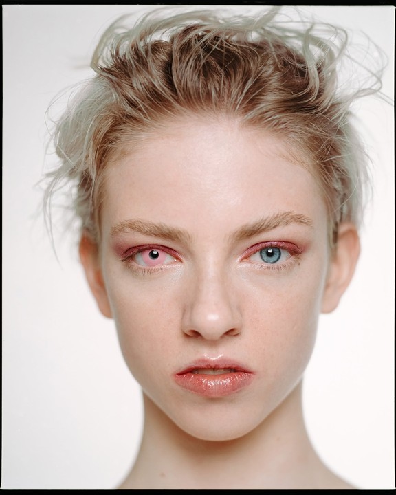 A woman with pink and blue eyes stares directly at the viewer.