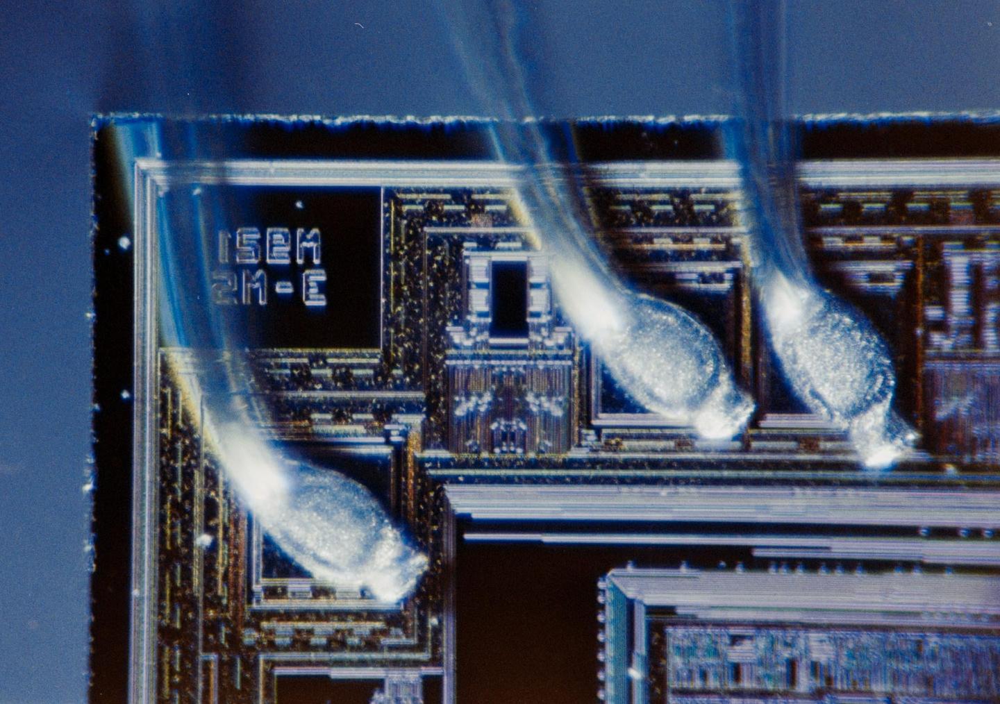A close-up view of an integrated circuit shows intricate patterns and three bright, glowing elements.