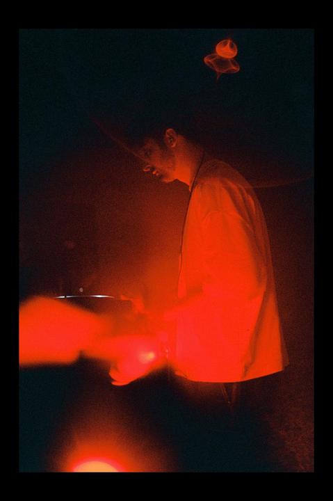 A man is illuminated by red light while DJing in a dark room.