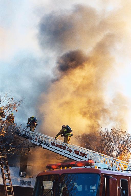 Firefighters climb a ladder from a fire truck into a cloud of smoke.