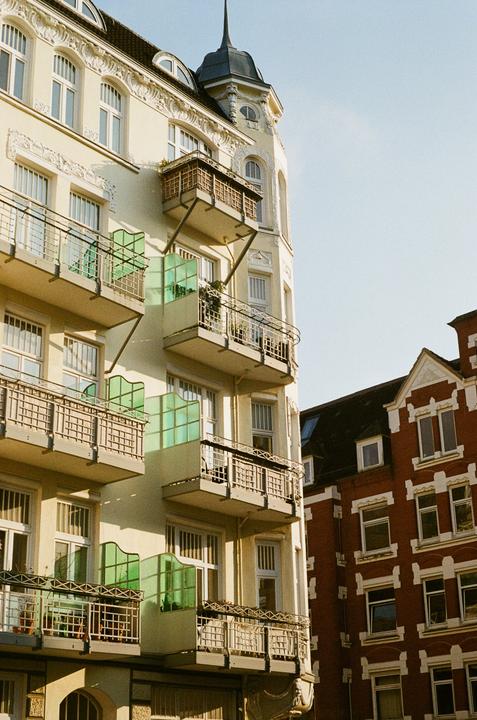 A cream-colored building with balconies and a turret stands next to a red brick building.
