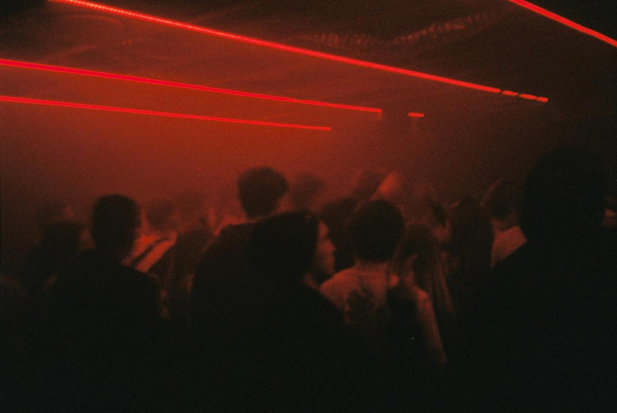 A crowd of people are visible in a dark room illuminated by red laser beams.