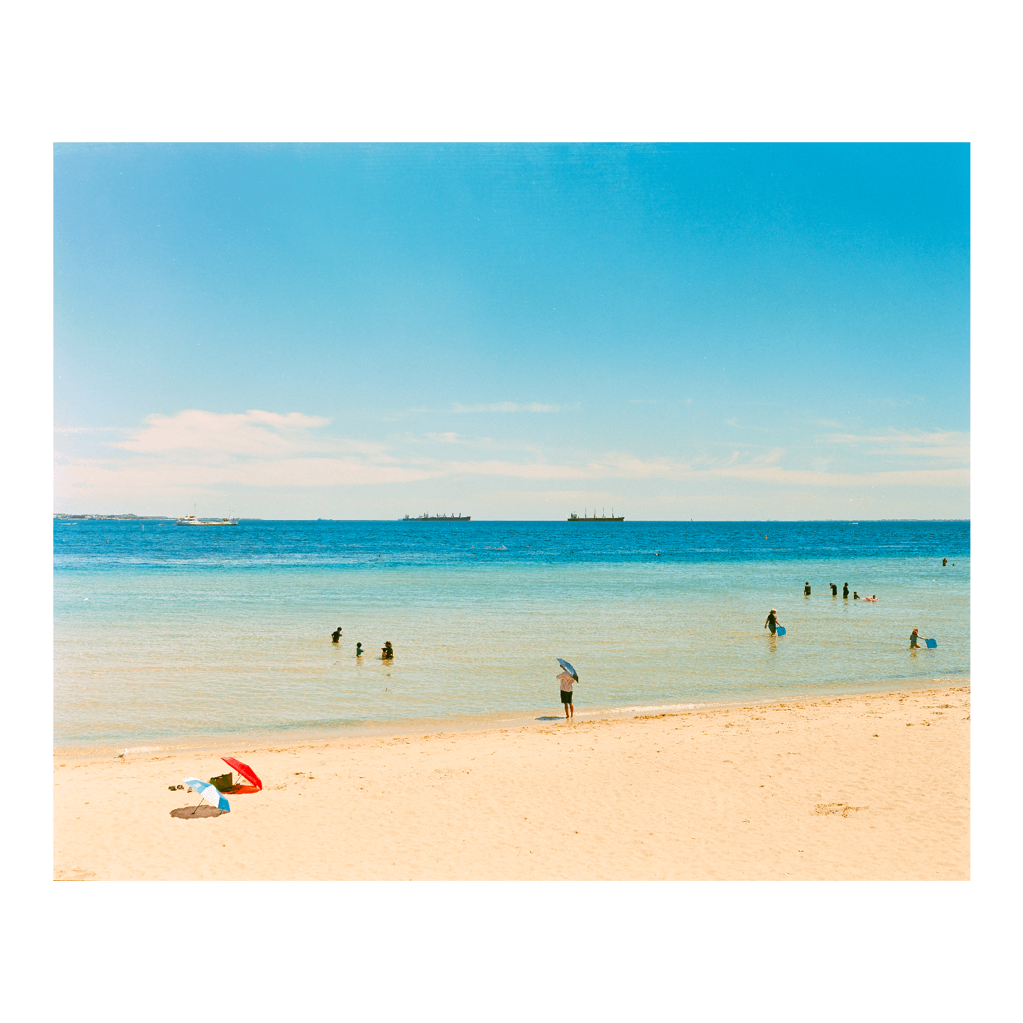 A wide shot shows a beach with people in the water and two umbrellas on the sand.