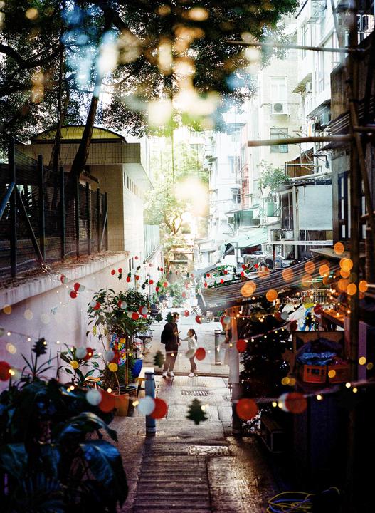 A man and a girl stand on a narrow street decorated with festive lights and ornaments.