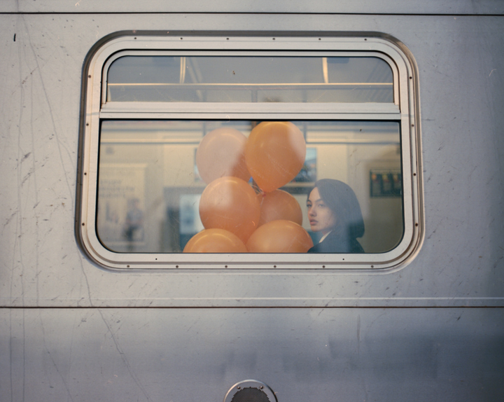 A woman with balloons looks out of a train window.