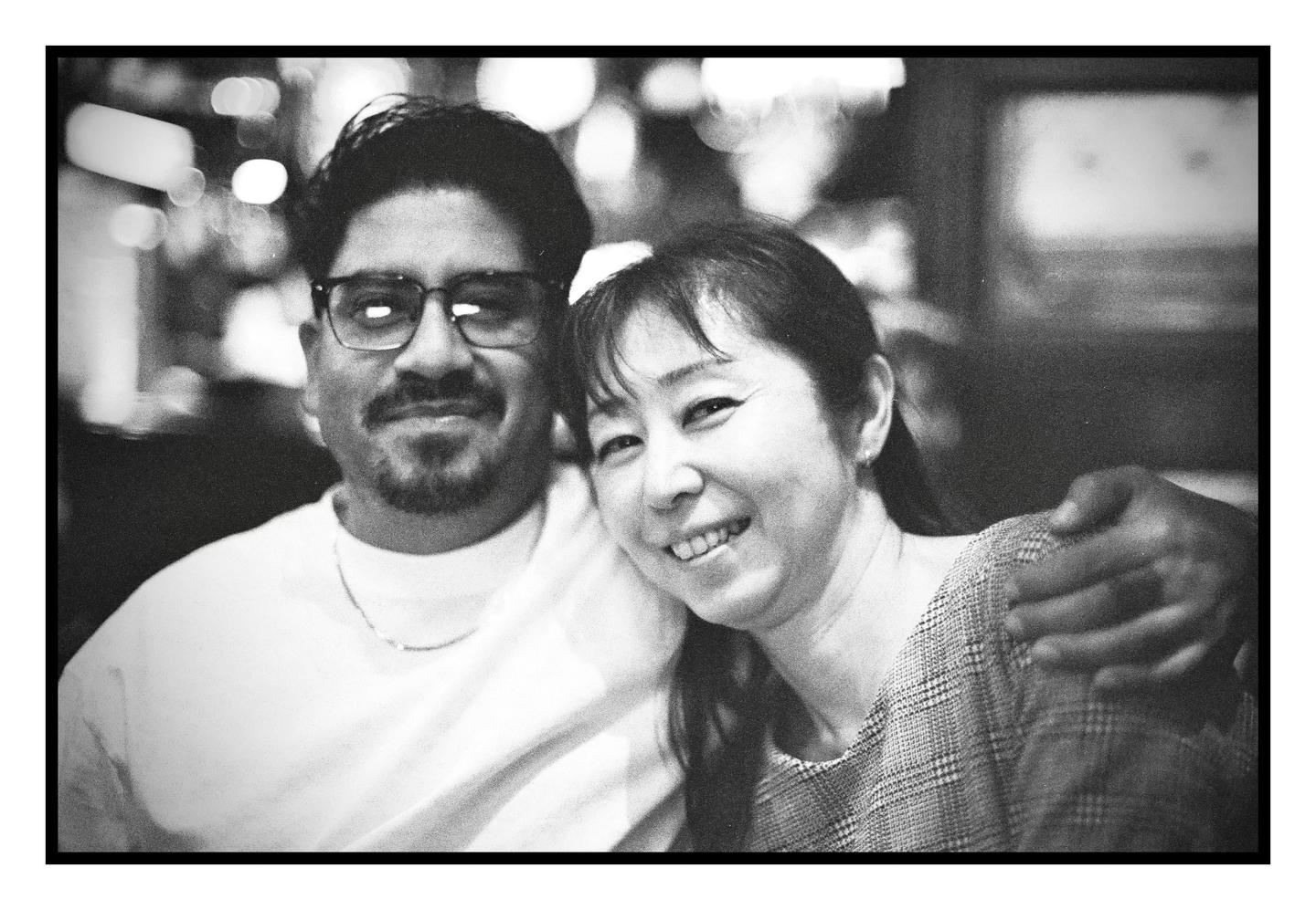 A man and a woman are smiling at the camera, with the man's arm around the woman.