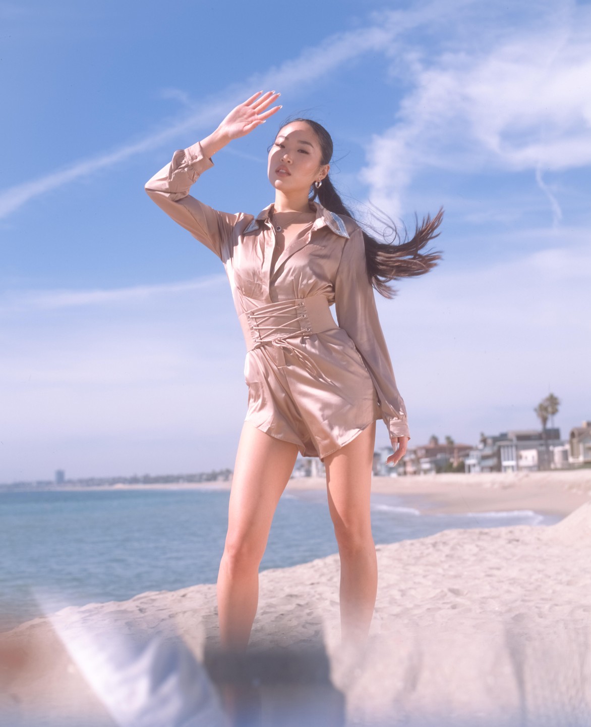A woman stands on a sandy beach, shielding her eyes from the sun.