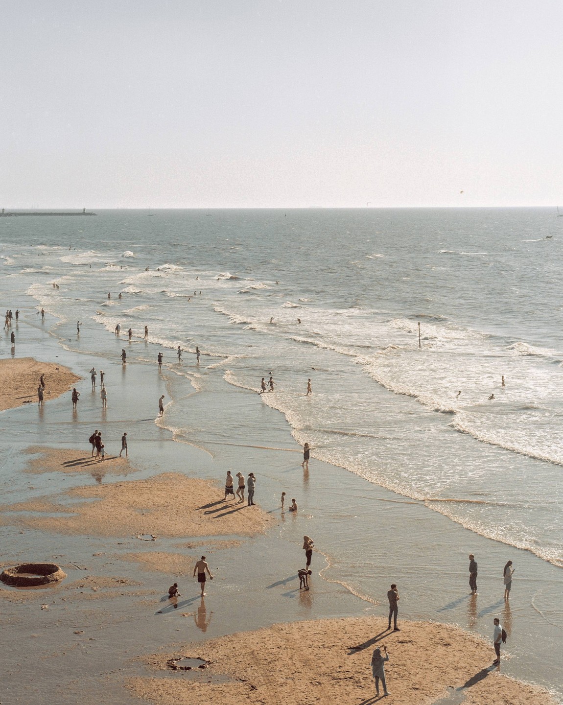 Many people are on a beach with waves rolling in from the ocean.