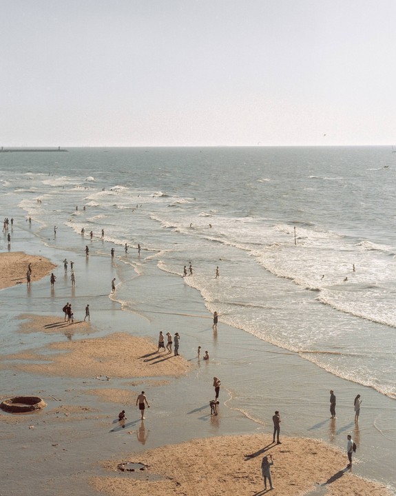 Many people are on a beach with waves rolling in from the ocean.