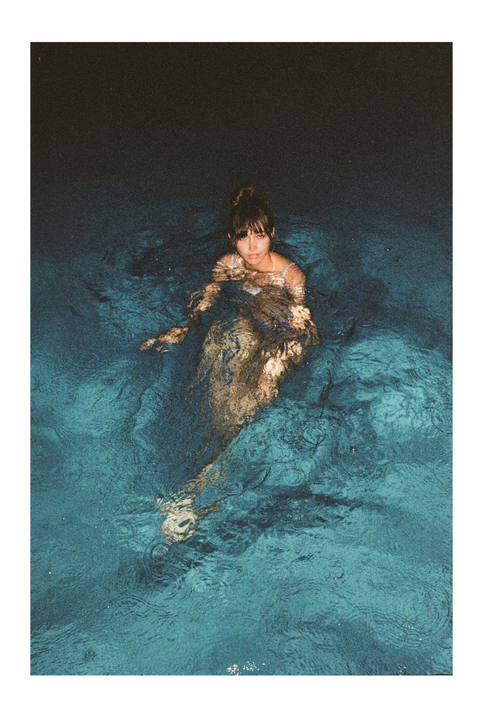 A woman with her hair in a bun is partially submerged in dark blue water with ripples on the surface.