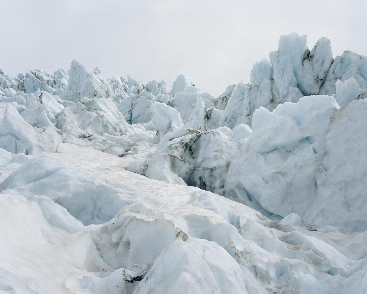 A vast expanse of a glacier with jagged ice formations and snow is visible under a bright sky.
