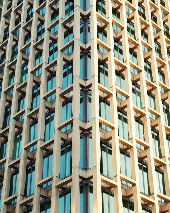 A modern building with a grid-like facade and blue-tinted windows is shown from a low angle.