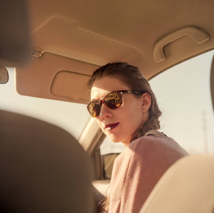 A woman wearing sunglasses looks over her shoulder from the driver's seat of a car.
