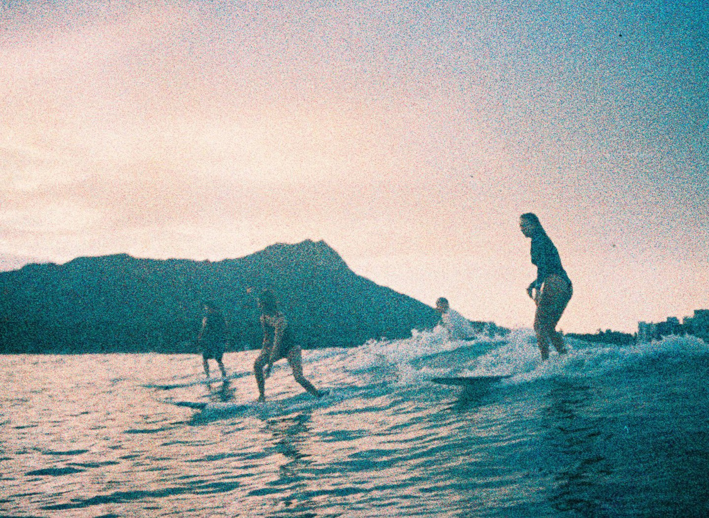 Three people are surfing on waves with a mountain in the background.