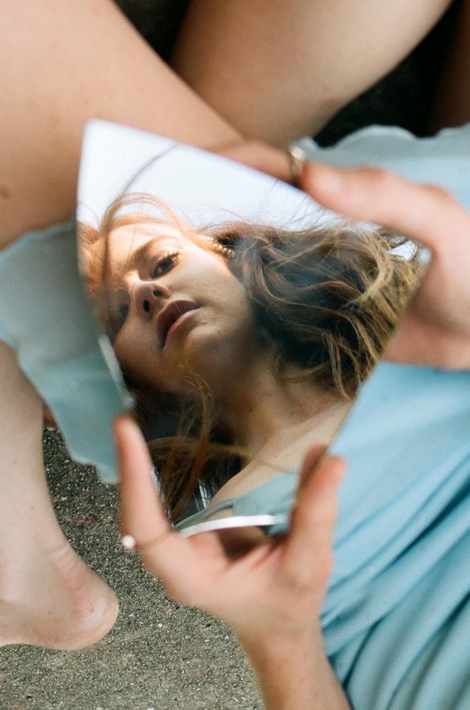 A woman's face is reflected in a small, irregularly shaped mirror held in her hand.