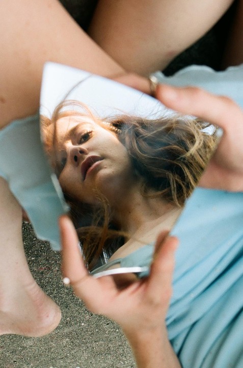 A woman's face is reflected in a small, irregularly shaped mirror held in her hand.