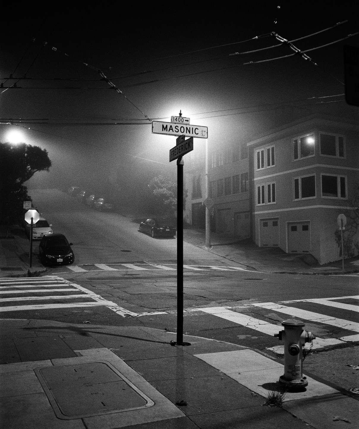 A street sign for Masonic and Frederick stands at a foggy intersection at night.