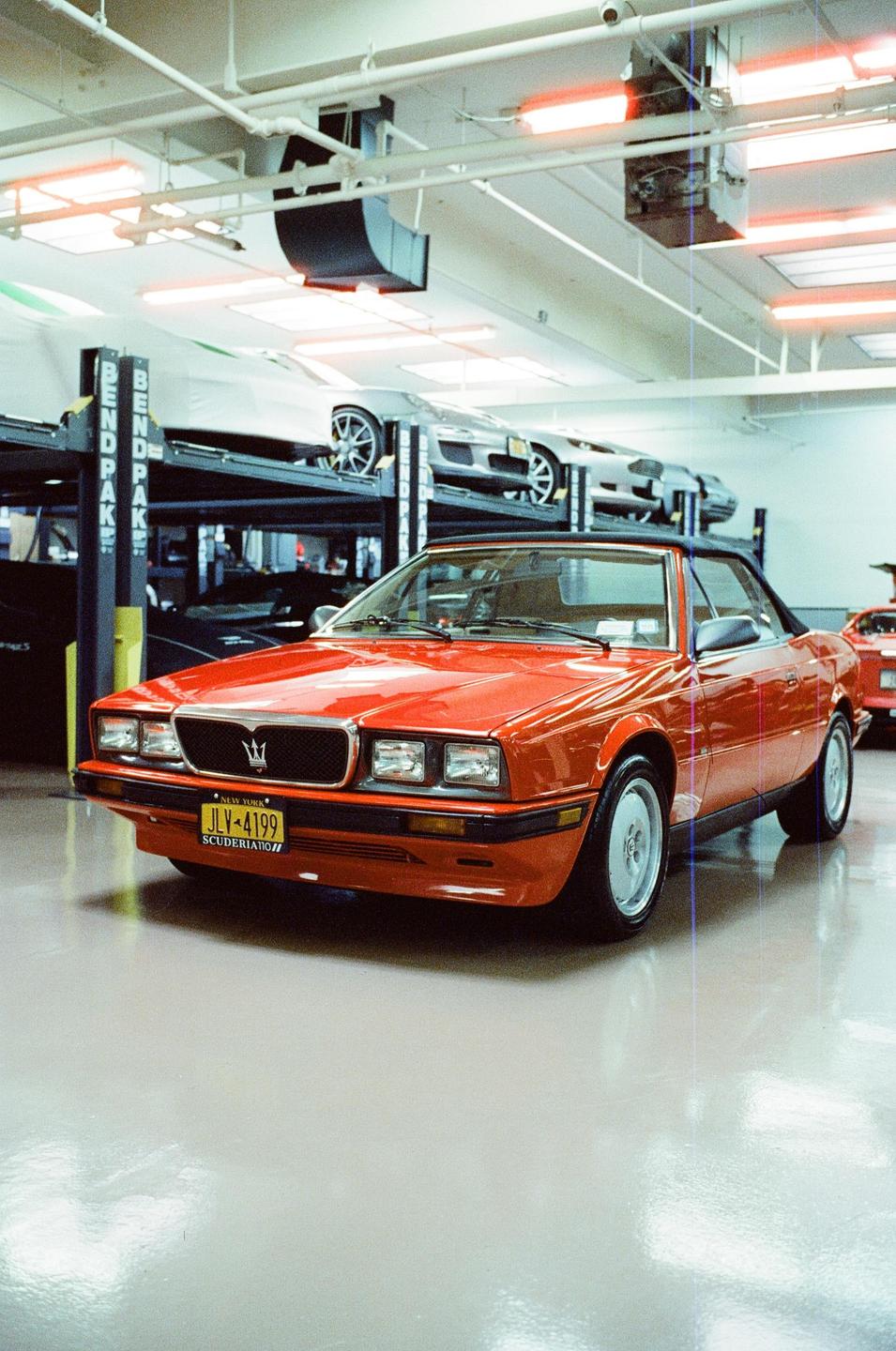A red convertible car is parked in a garage with other cars on lifts in the background.