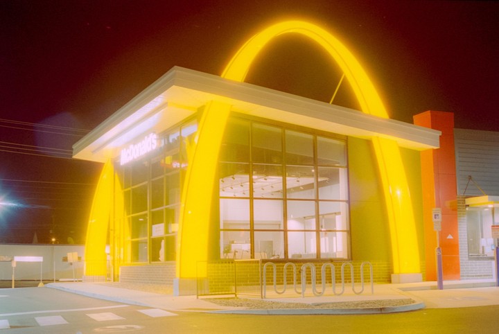 A McDonald's restaurant is brightly lit at night, with its golden arches glowing against the dark sky.