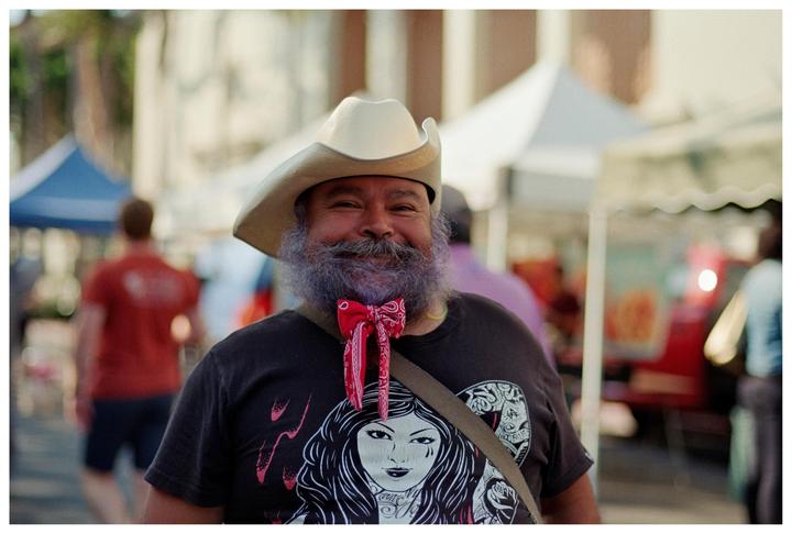 A man with a purple beard and a cowboy hat smiles at the camera.