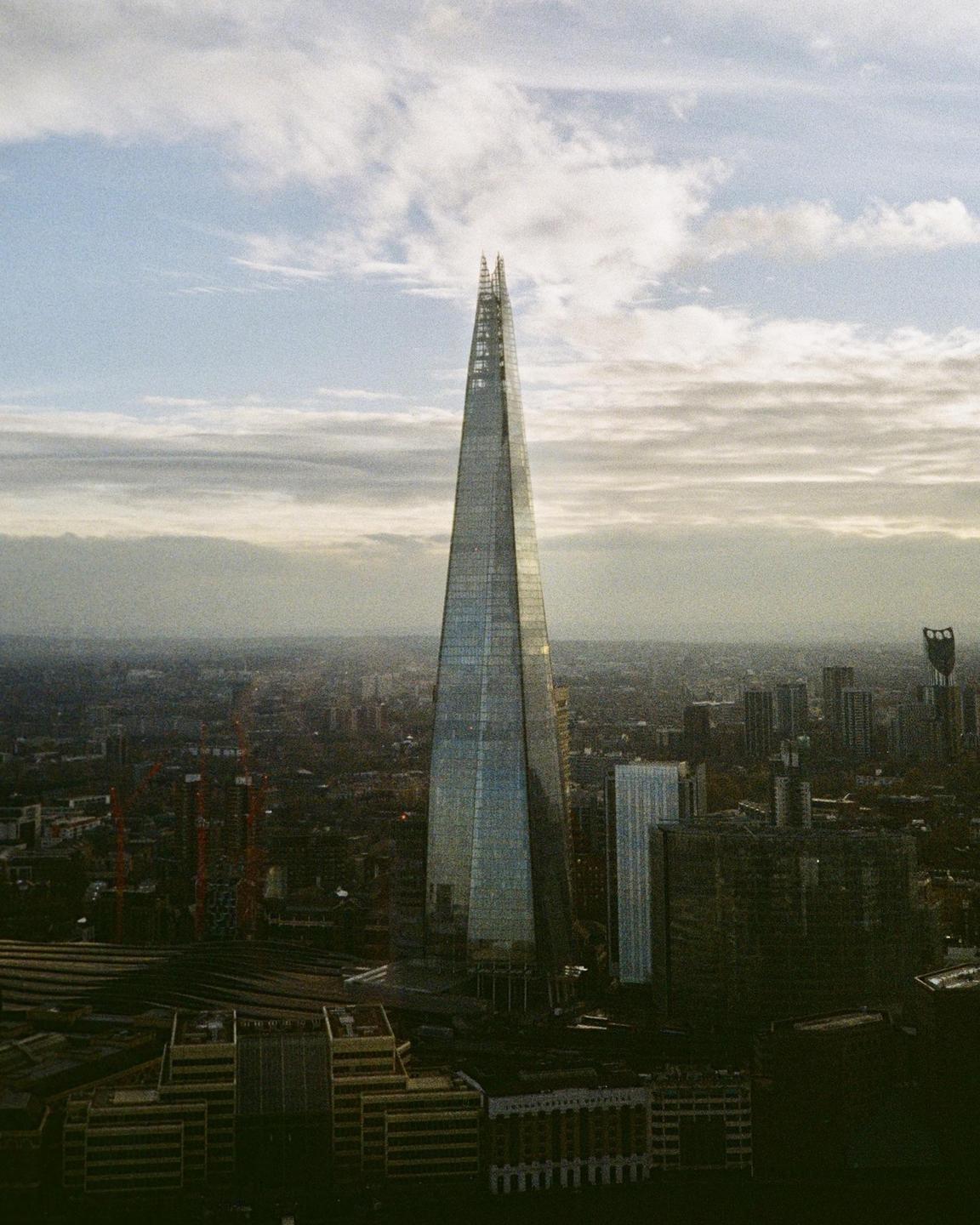 The Shard skyscraper stands tall over the city of London under a cloudy sky.