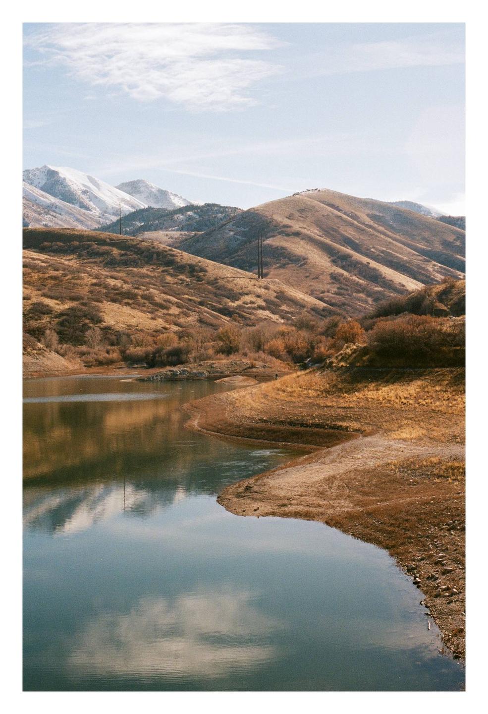 A body of water reflects the sky and is surrounded by hills, some of which are snow-capped.