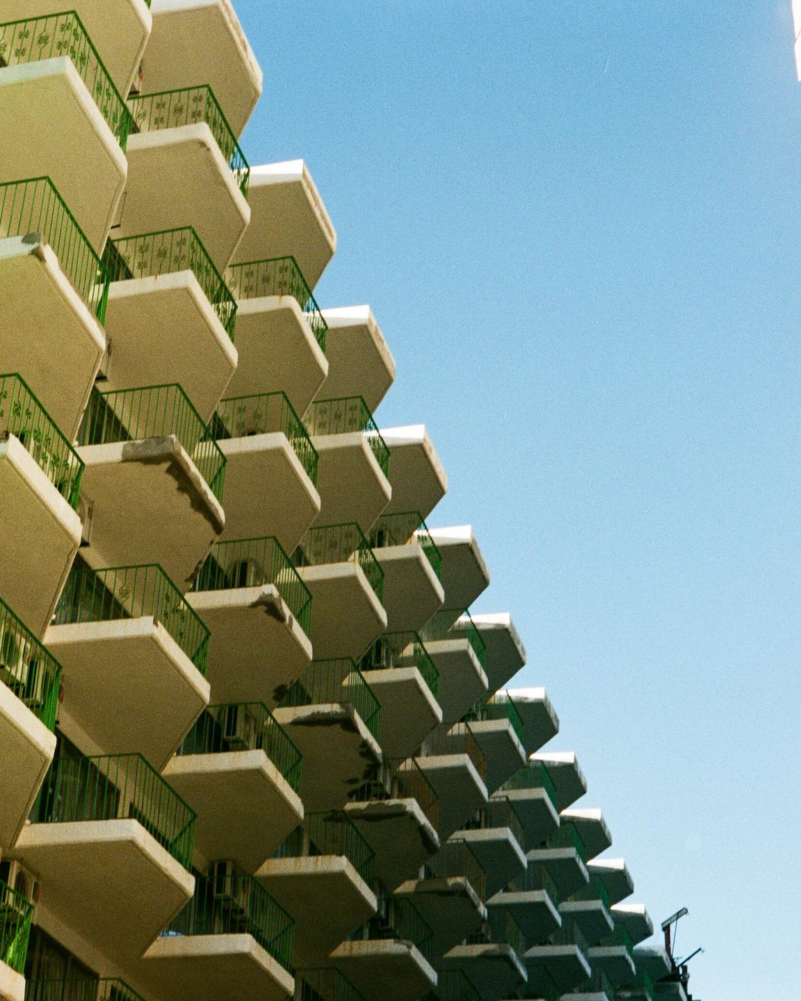 A hotel building with many balconies is shown against a clear blue sky.