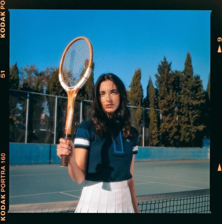 A woman in a tennis outfit holds a tennis racket on a tennis court.